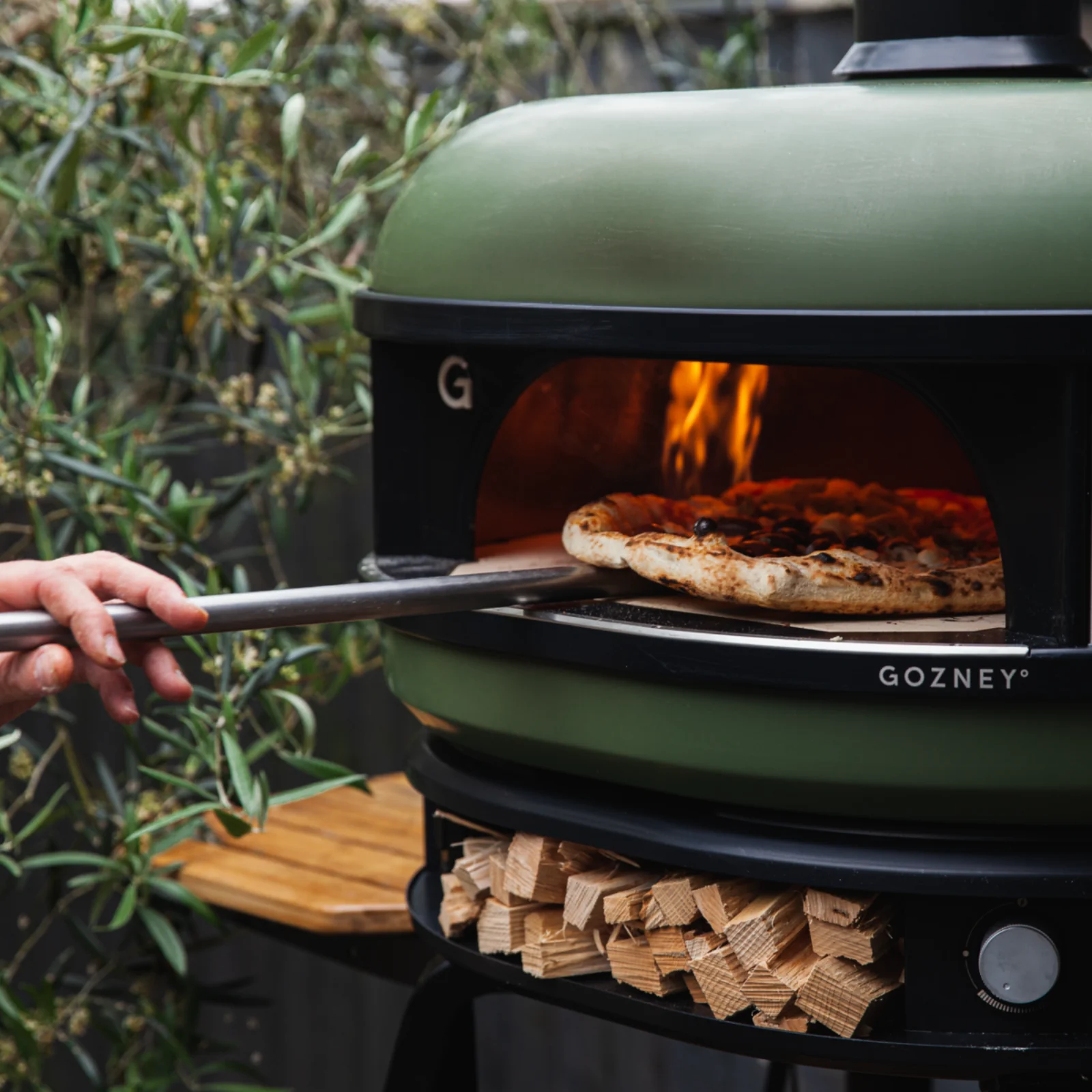 Pizza being placed inside Gozney Dome Olive Pizza Oven